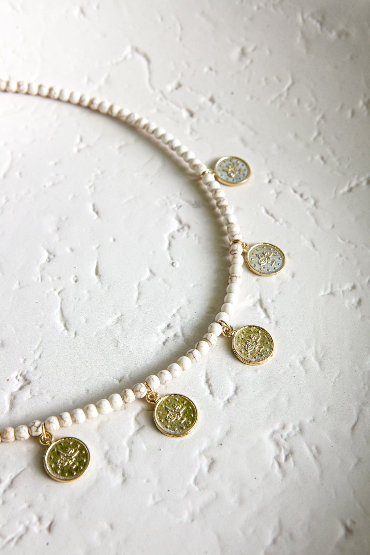 Beaded necklace with ivory-white beads and gold-toned coin pendants featuring green and pale inlays, from collections of necklaces.