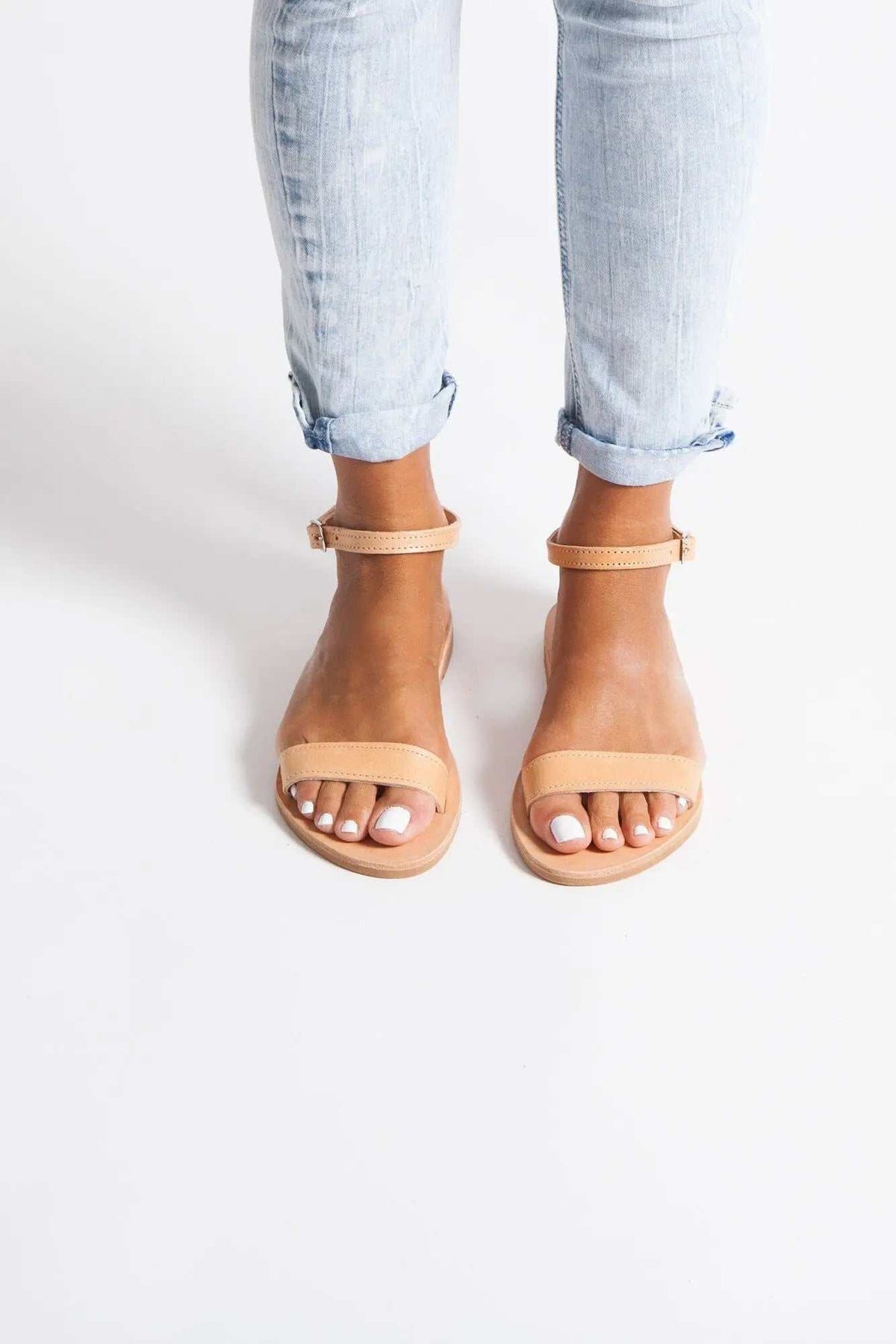ELIA Handmade Greek Sandals in natural tan leather with slim straps, ankle buckles and flat soles, worn with cuffed jeans