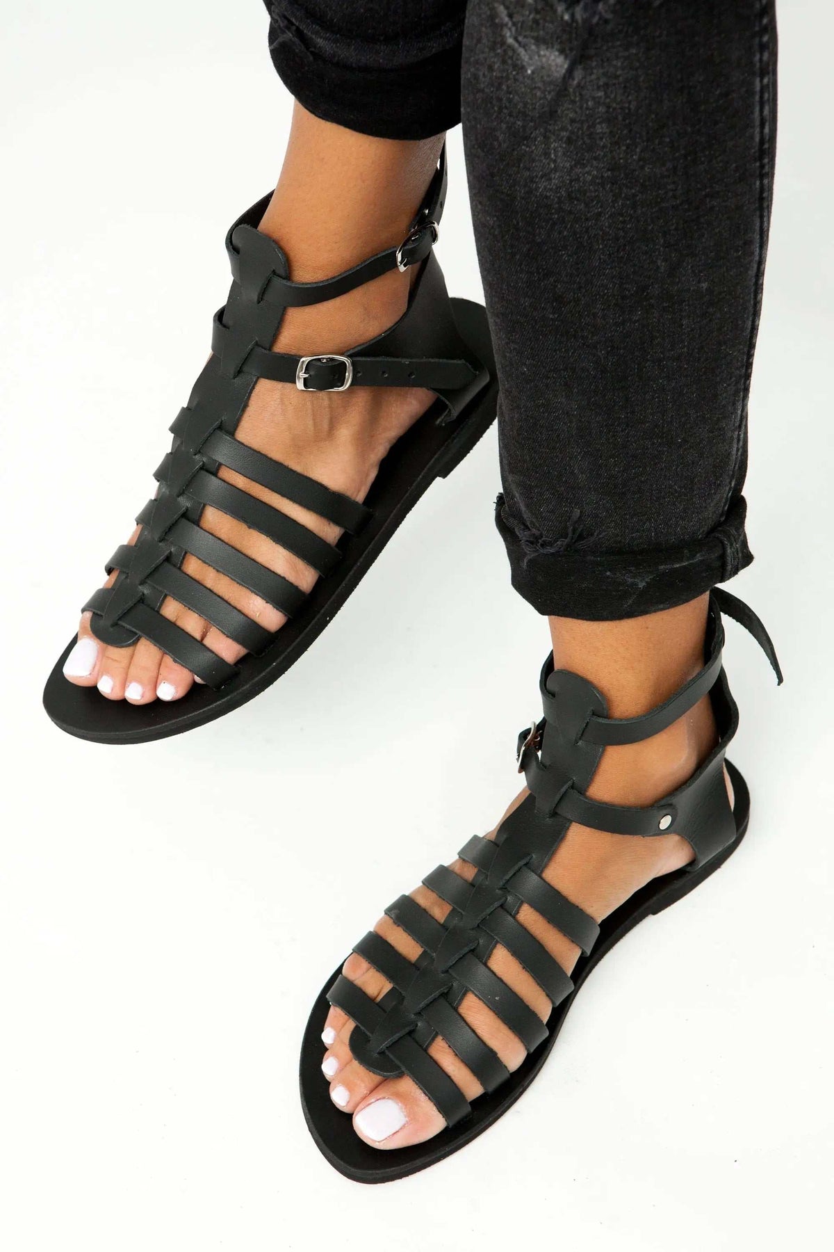 OLYMPE Handmade Greek Sandals in black leather, featuring multiple woven straps and buckled ankle straps with a flat sole