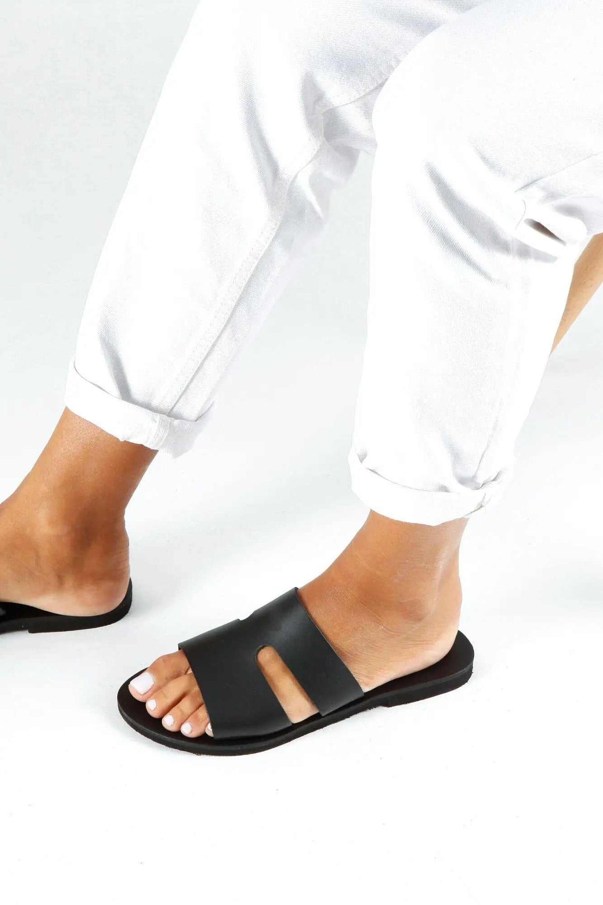 VOTSALO Handmade Greek Sandals in black leather with a wide toe strap and open sides, worn as flat slip-ons