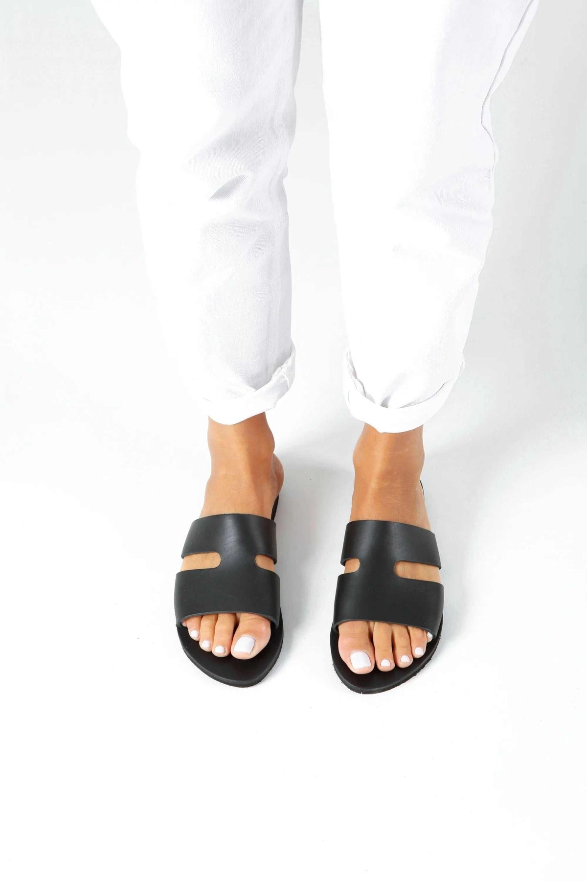 VOTSALO Handmade Greek Sandals, black leather flat sandals with wide straps and small cutout details across the toes.