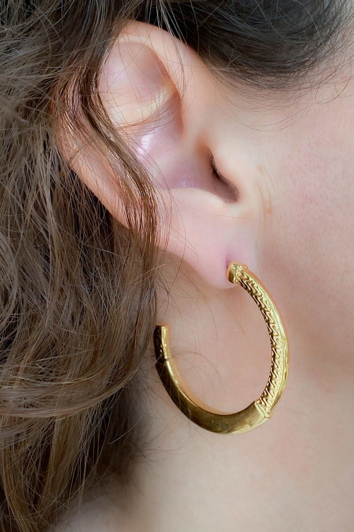24 k gold filled hoops in shiny gold-tone metal with raised tribal pattern and hinged closure