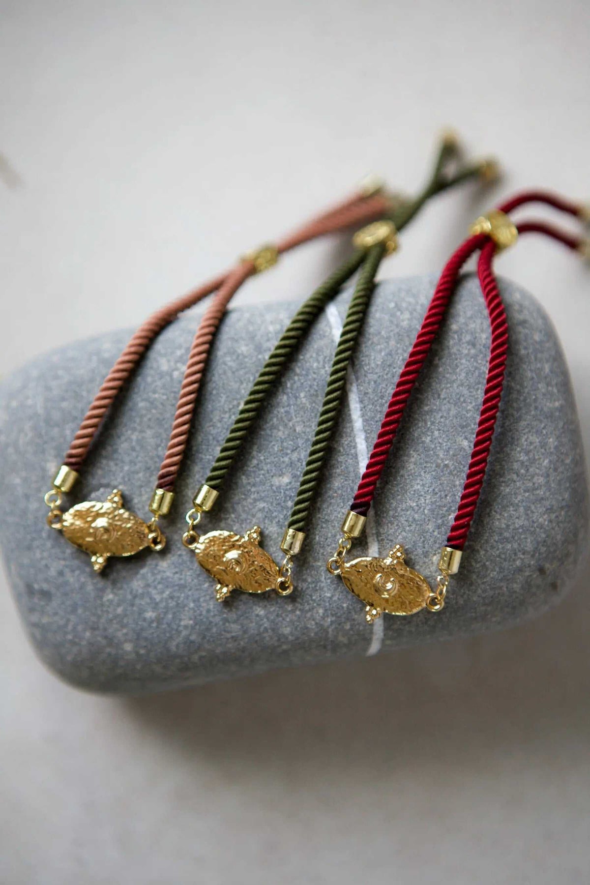 Adjustable rope Bracelet in red, green and salmon twisted cords, each with a textured gold-tone animal motif charm.