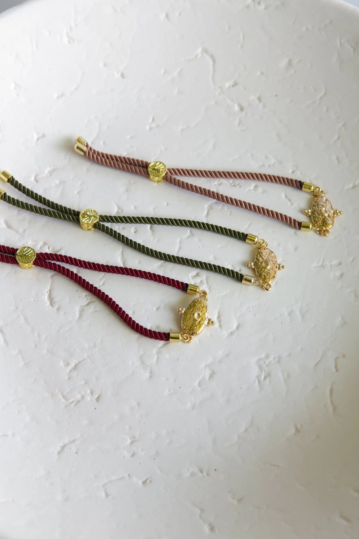 Adjustable rope Bracelet in red, khaki green and salmon cords, each with gold-tone medallion and ornate charm details