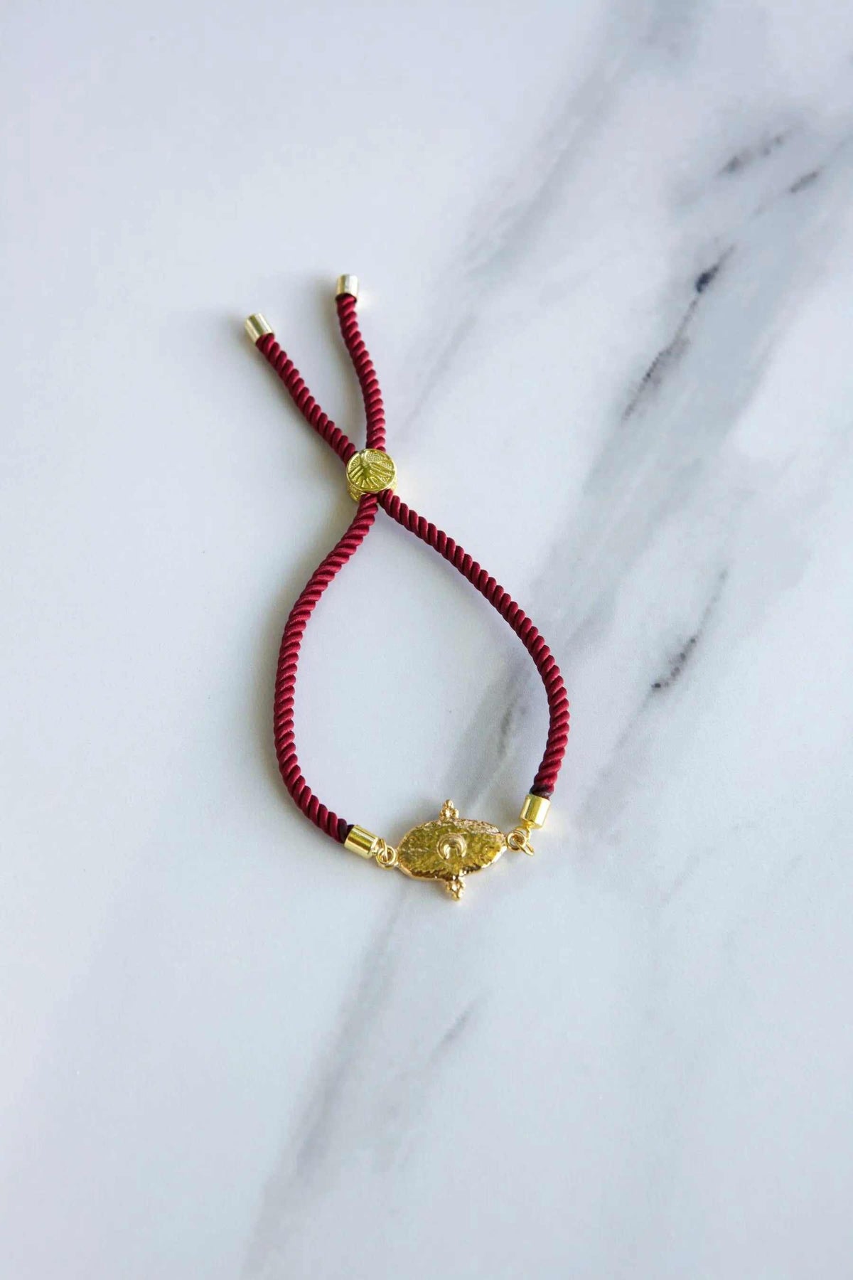 Adjustable rope Bracelet in red woven cord with gold-tone tribal centerpiece, sliding knot and metal end caps