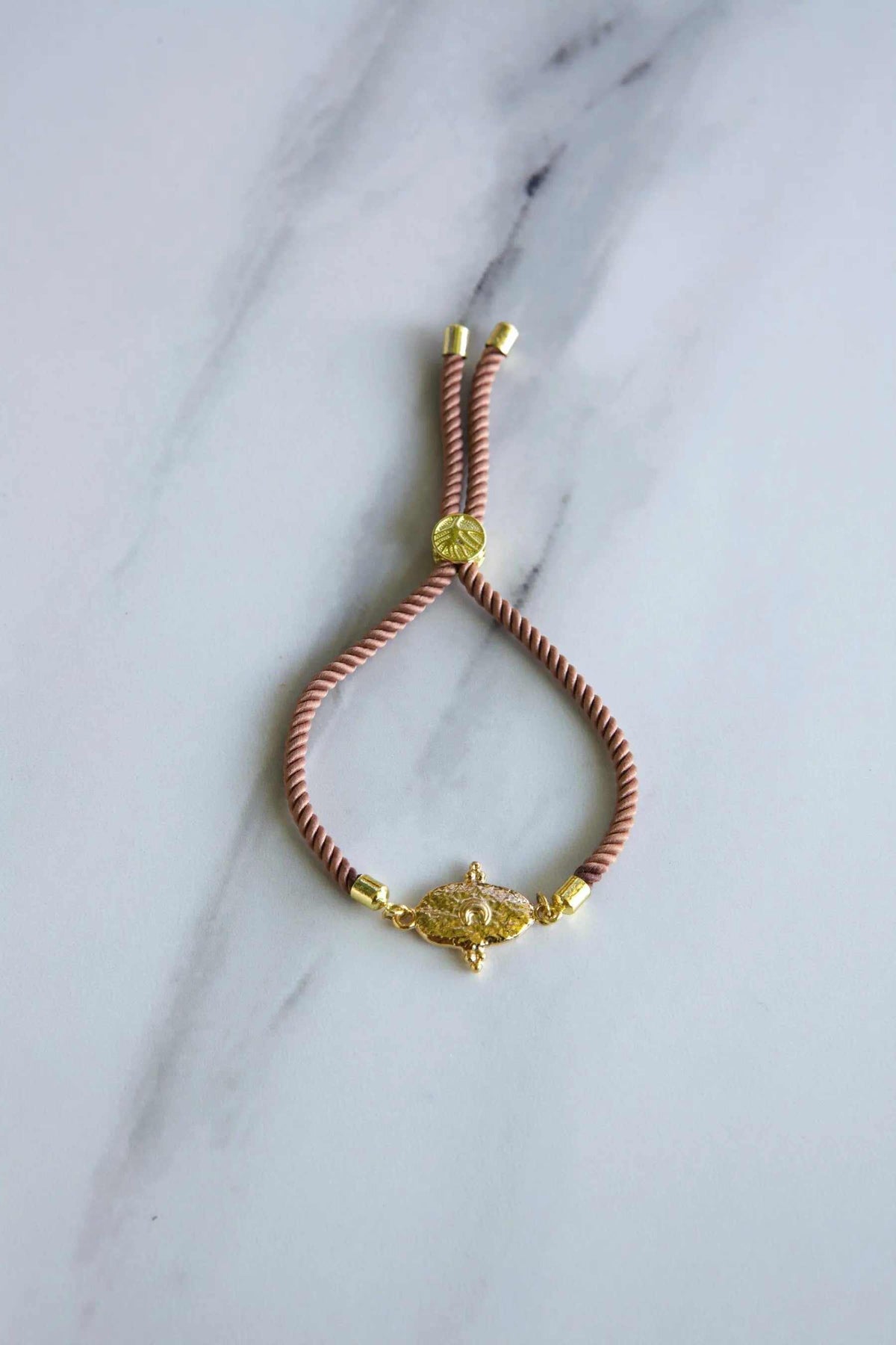 Adjustable rope Bracelet in salmon-pink twisted cord with gold-tone end caps, round accent and ornate tribal centerpiece