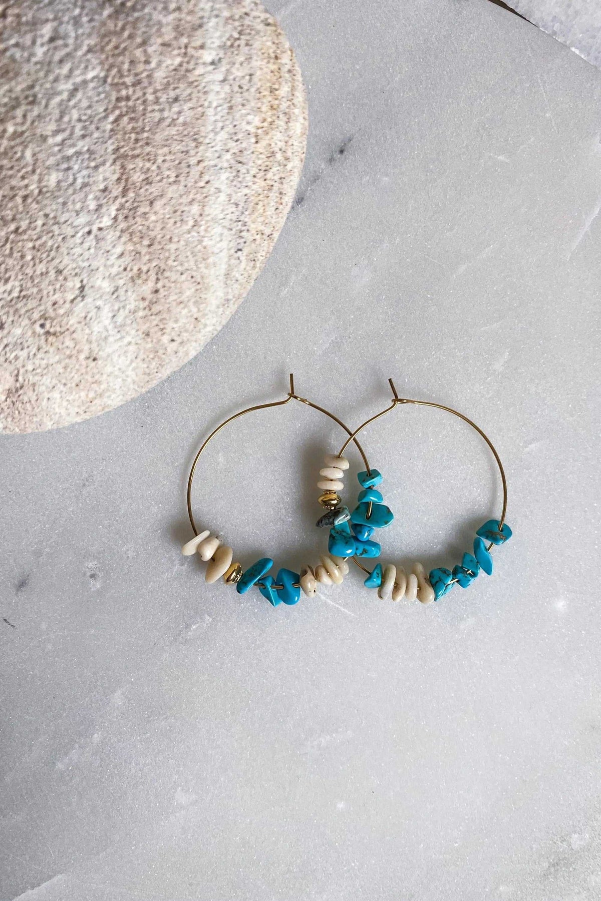 AFRODITA EARRINGS are gold-tone hoop earrings with turquoise-blue and cream irregular chip stones along the lower edges
