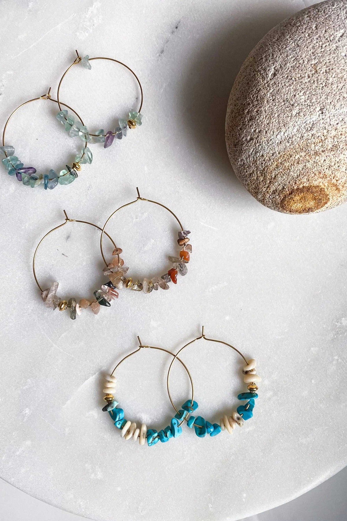 AFRODITA EARRINGS are thin gold-tone hoops decorated with irregular turquoise, purple, green, and earthy stone chips