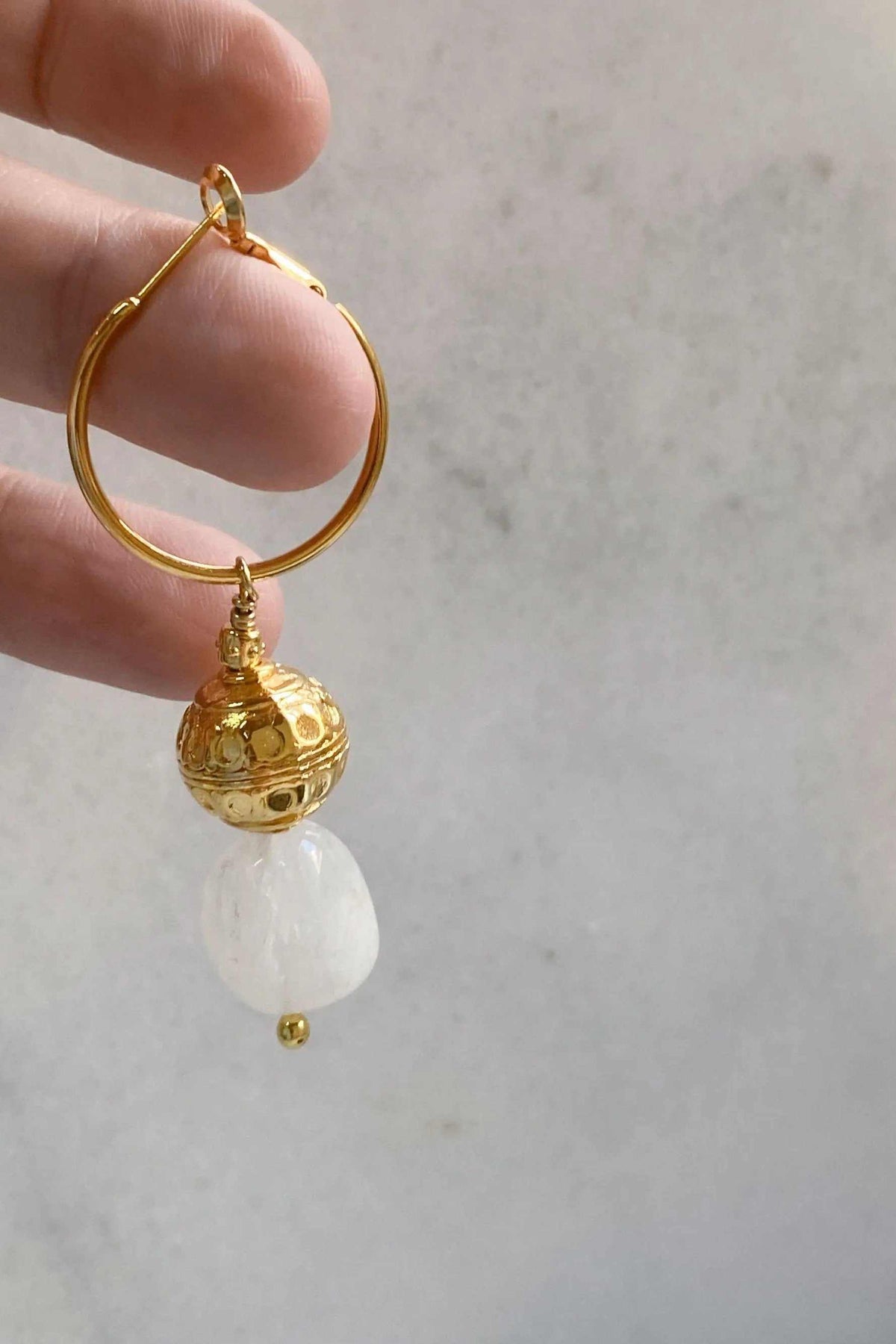 AGAPE EARRINGS featuring a gold-tone hoop with an ornate textured charm and a white translucent stone drop