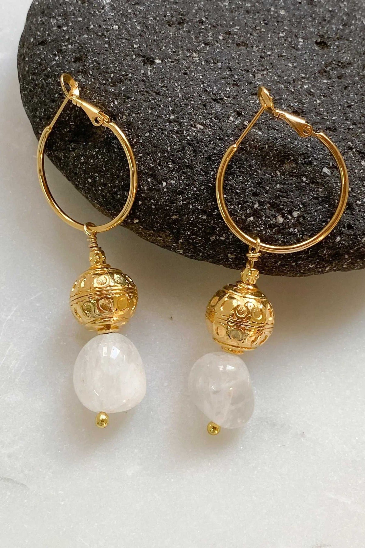 AGAPE EARRINGS are gold-tone hoop earrings with ornate spherical charms and milky white irregular stones