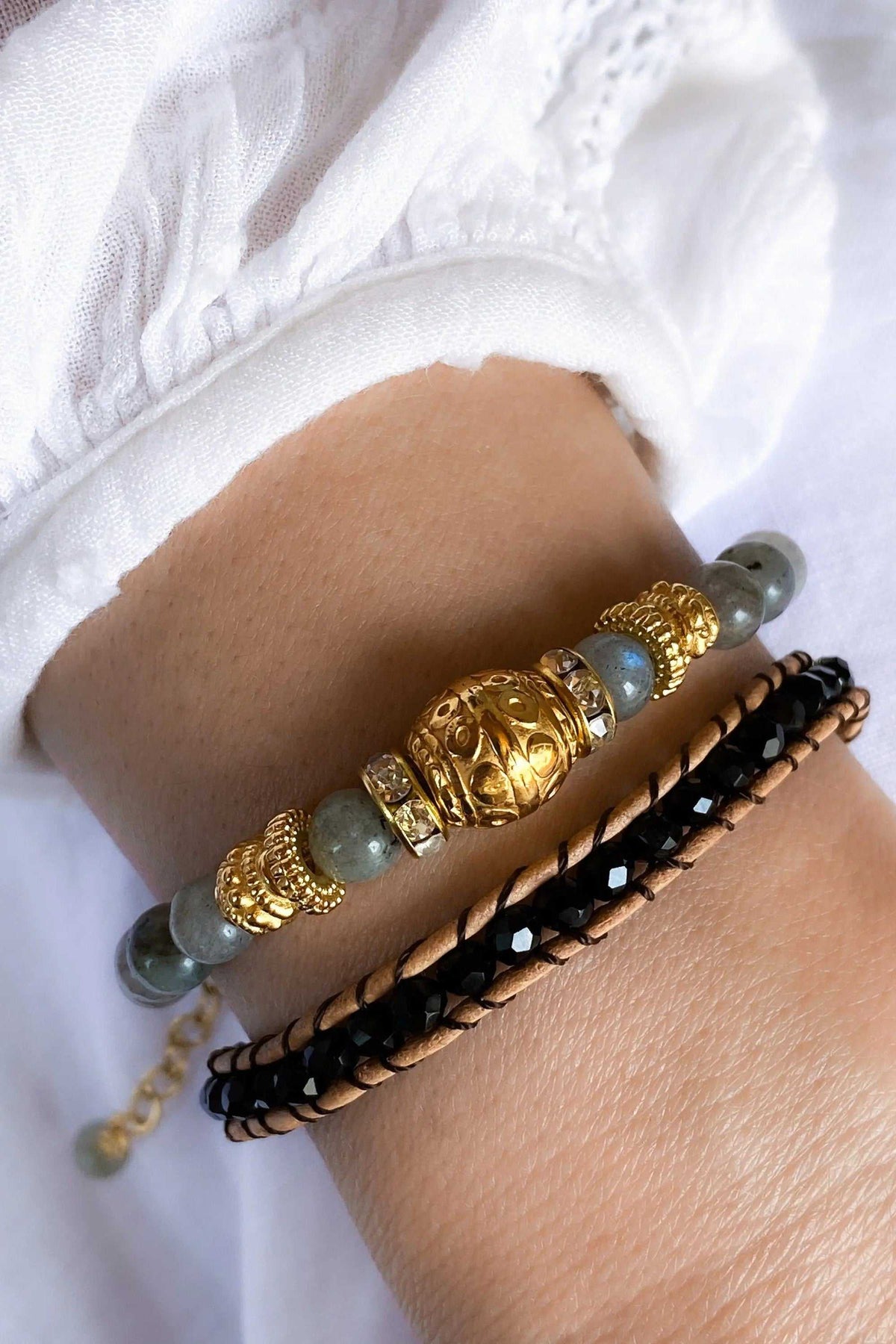 AGAPI BRACELET set with black braided leather and a grey-green crystal bead strand, accented by ornate gold-tone beads