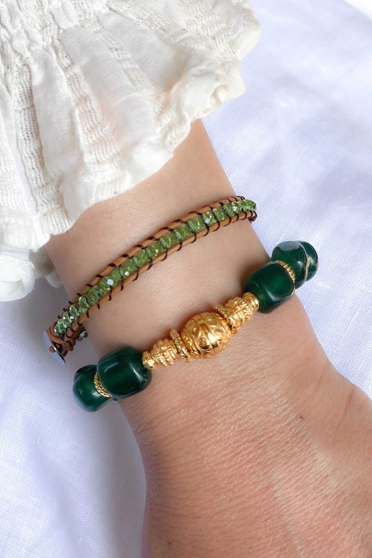 AGAPI BRACELET with green crystal beads woven into brown leather, alongside dark green stones and a gold-tone centerpiece