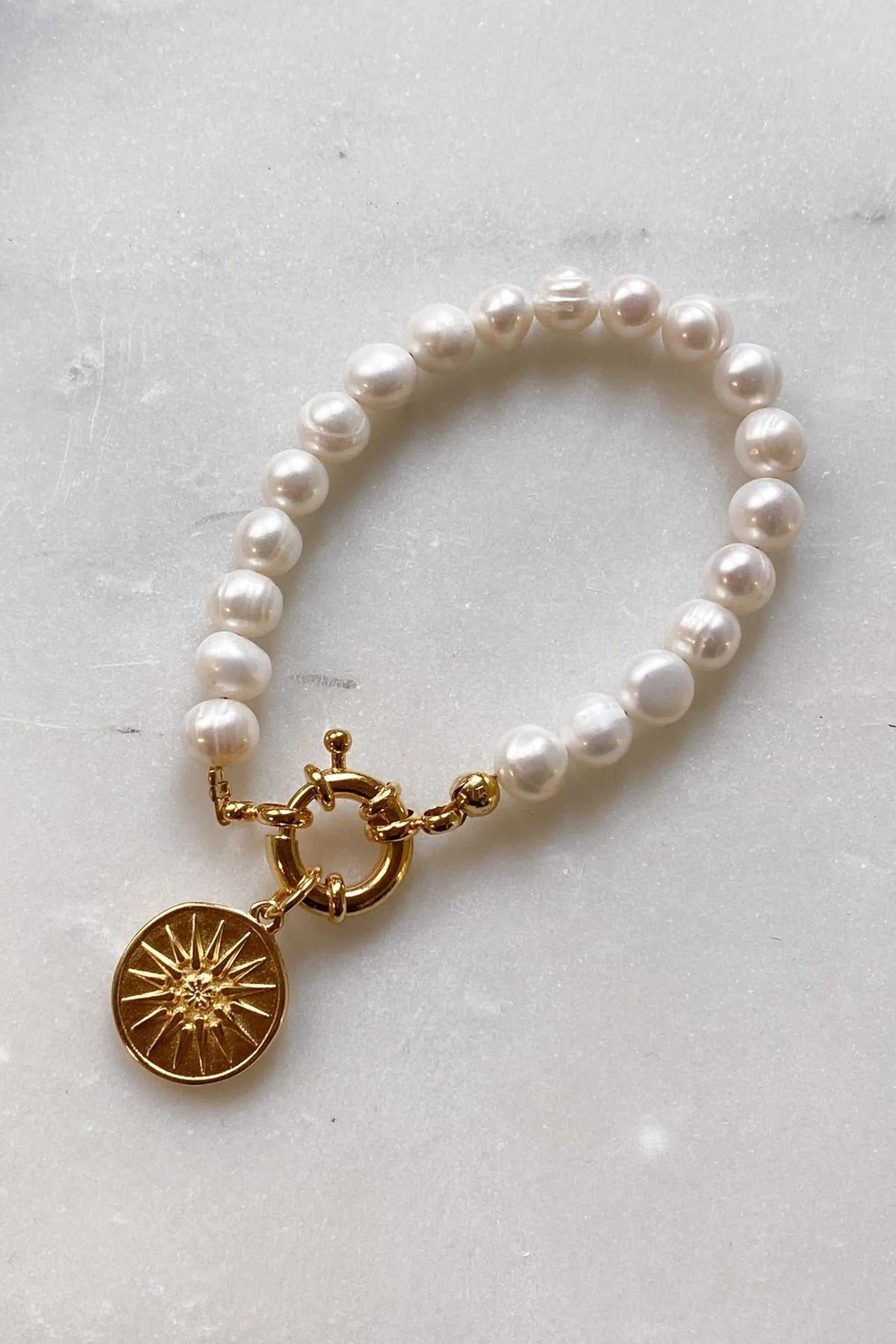 Pearl bracelet featuring lustrous white freshwater pearls and a gold-tone Alexander the Great sunburst coin charm
