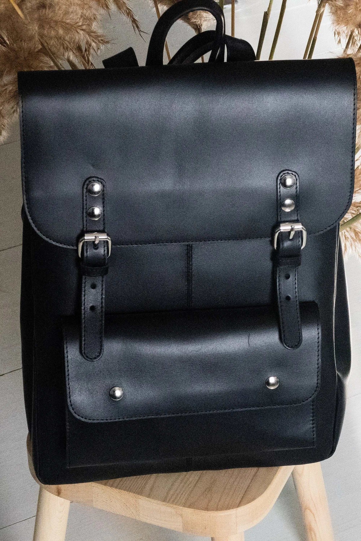 ALKION BACKPACK in black leather with a structured flap, twin buckle straps, large front pocket and top handle