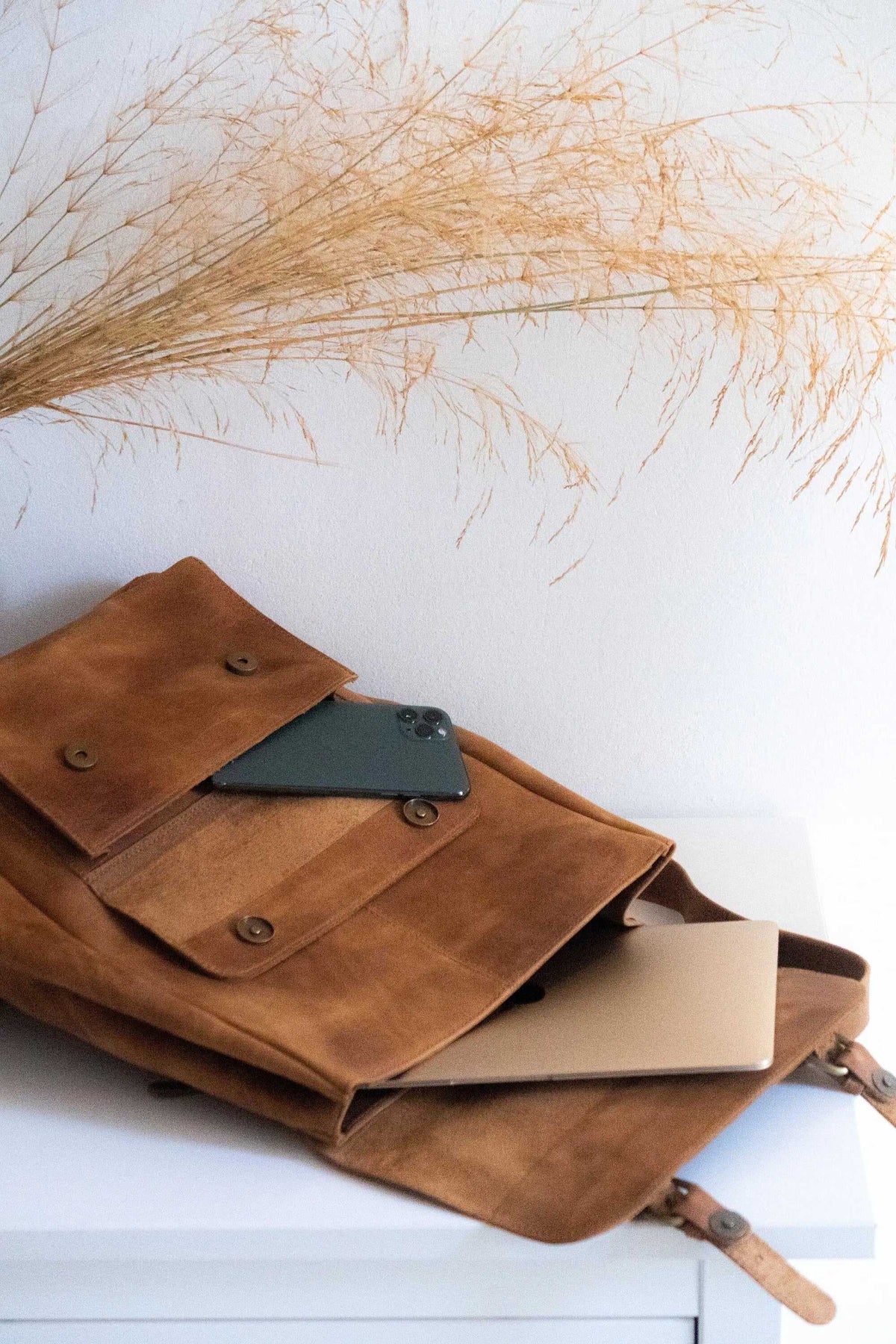ALKION BACKPACK in warm brown leather with a soft, textured finish, featuring a wide front pocket with snap closures and adjustable straps