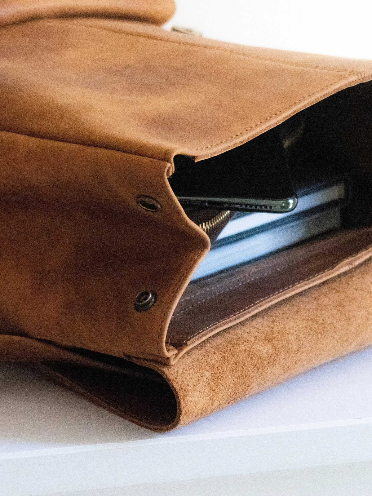 ALKION BACKPACK in mustard nubuck leather with a soft suede texture, metal snap fasteners and an open front pocket holding a phone and books