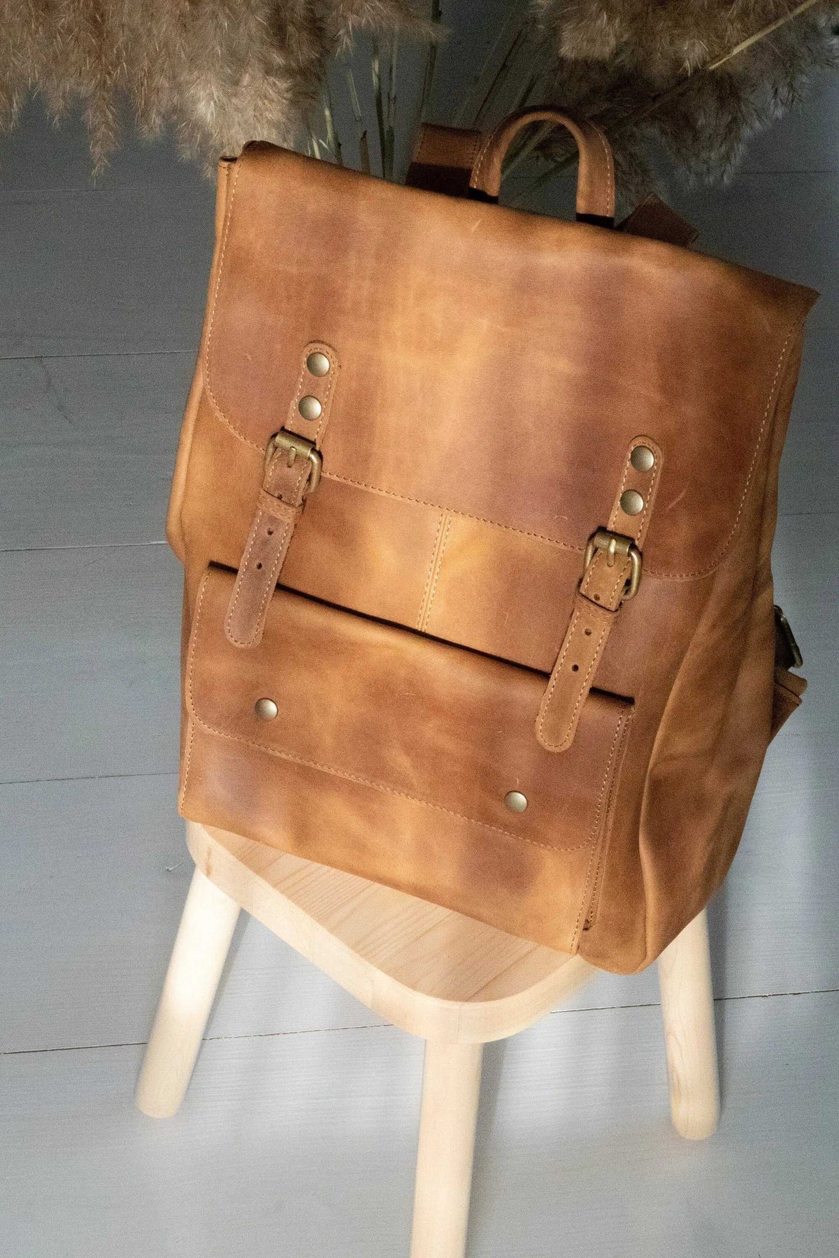 ALKION BACKPACK in warm tan full-grain leather with a structured flap, adjustable buckle straps and front pocket