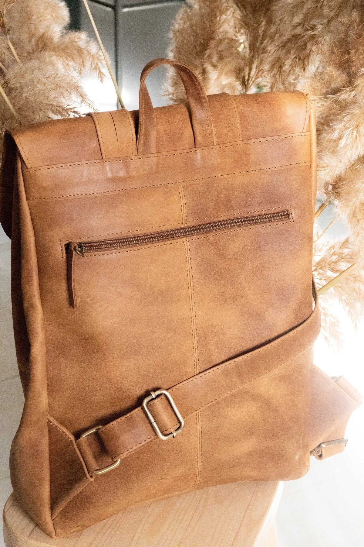 ALKION BACKPACK in tan full-grain leather with a smooth finish, top handles, front zip pocket and metal buckle strap
