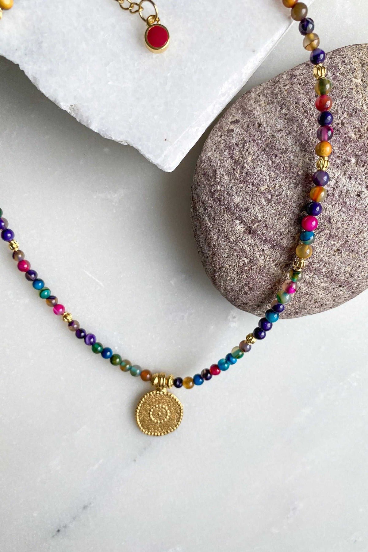 ALKYONI NECKLACE featuring colourful beaded agate-style strand with gold pendant and red bead clasp