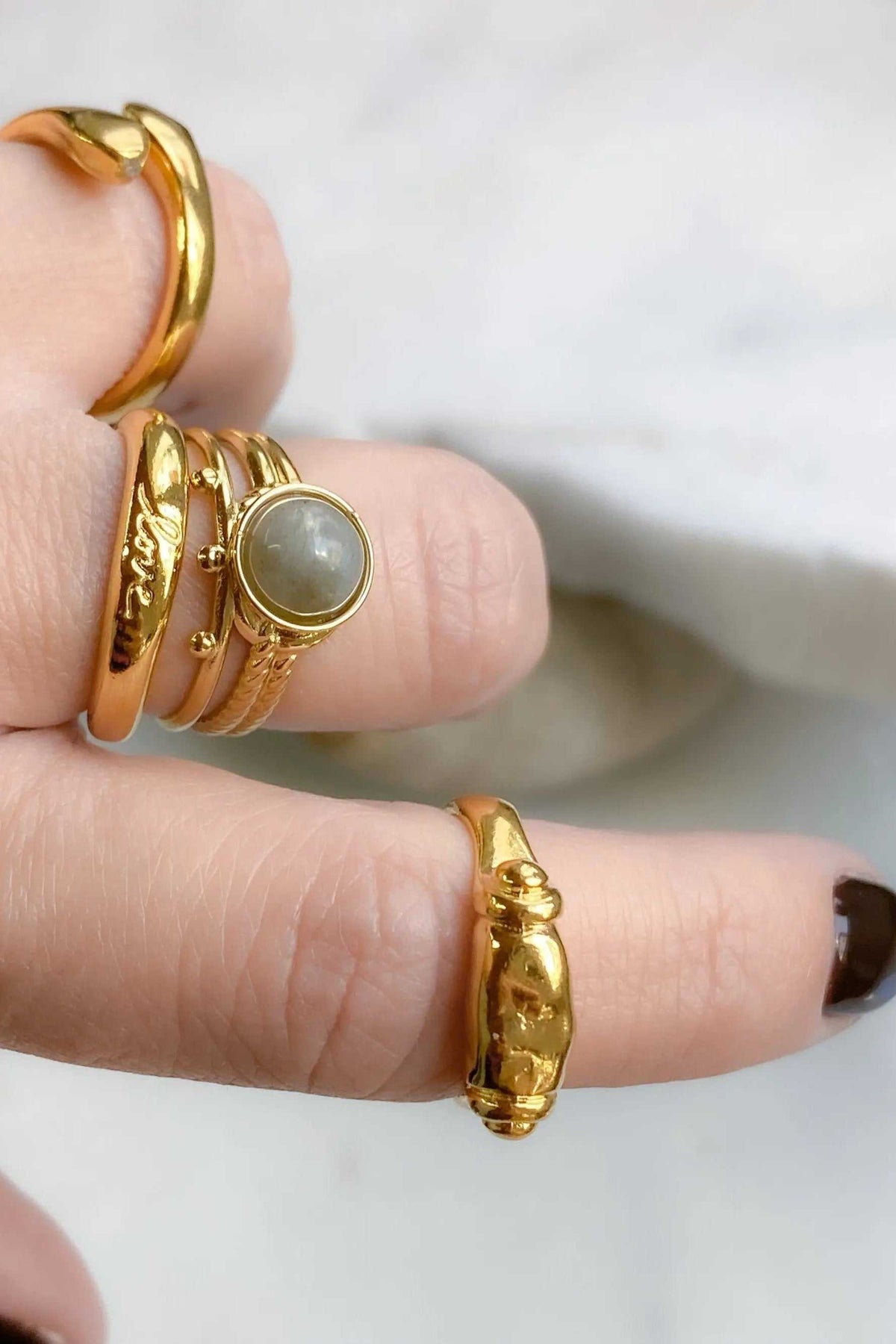 Ancient Greek ring set in shiny gold tones, featuring sculpted bands and a round pale grey stone centerpiece