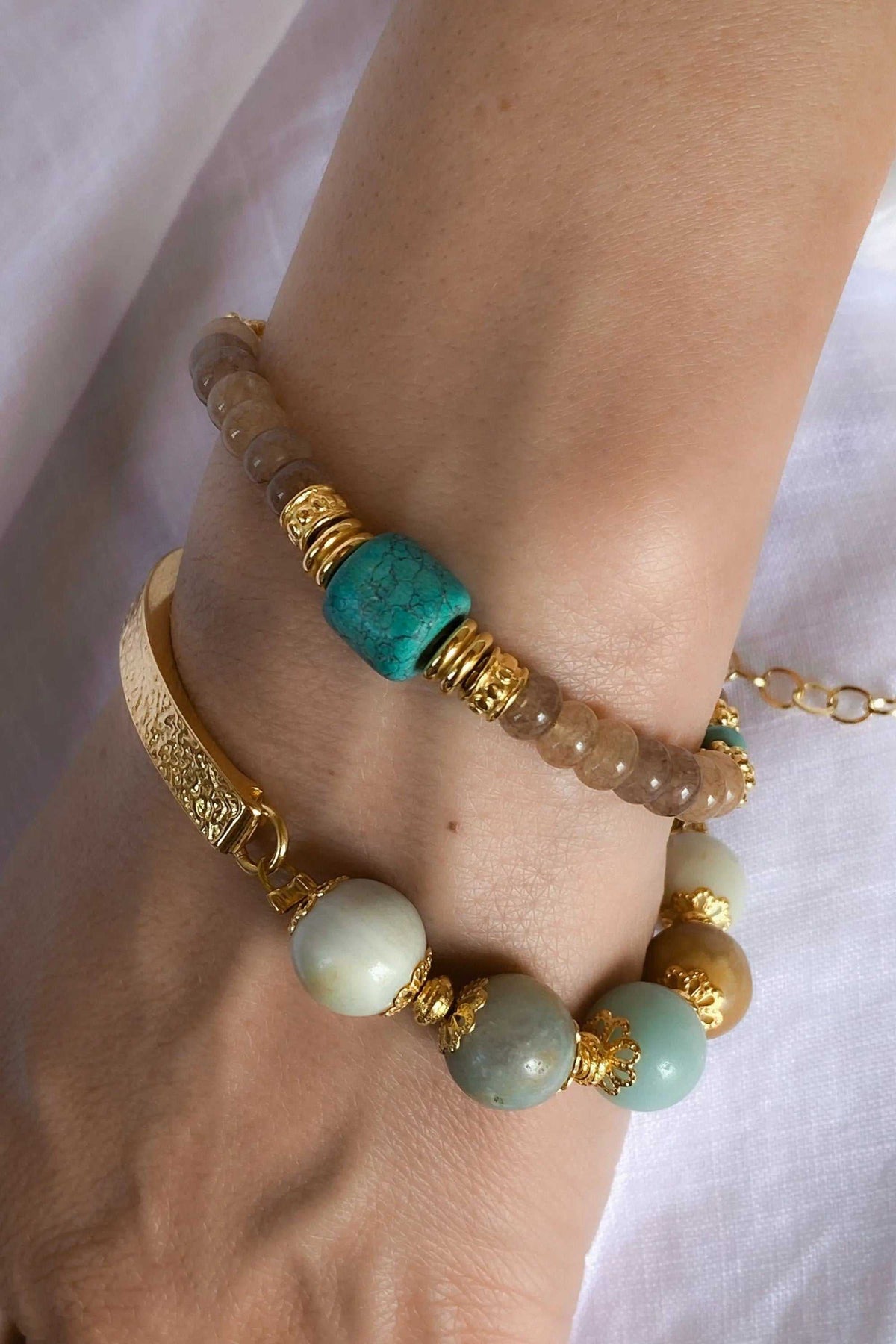 ARETI Bracelet with translucent brown agate beads, a vivid turquoise stone and gold-tone accents, worn beside a second beaded bracelet