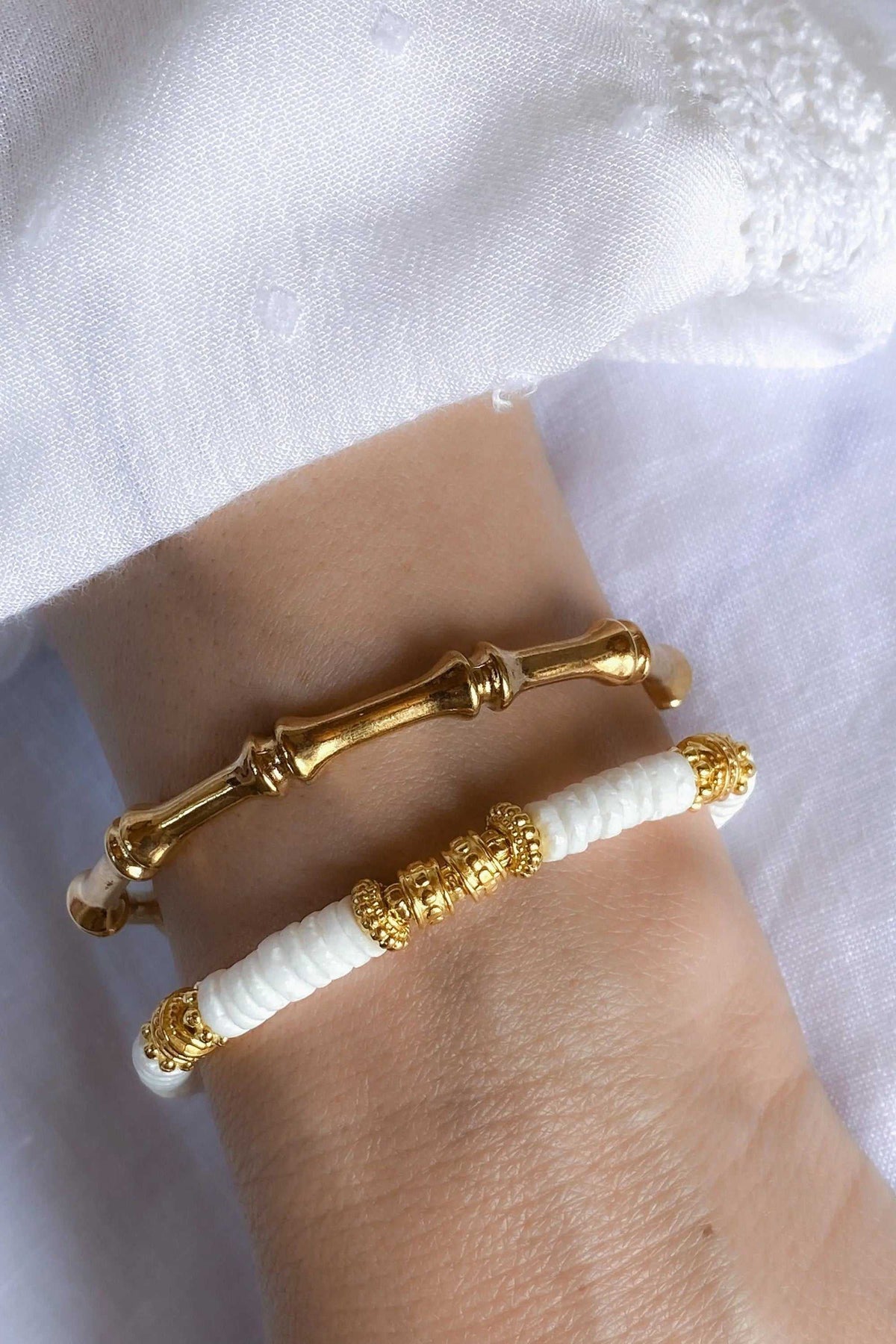 Bamboo pattern bracelet in polished gold tone with sculpted bamboo joints, shown beside a white beaded bracelet with gold accents