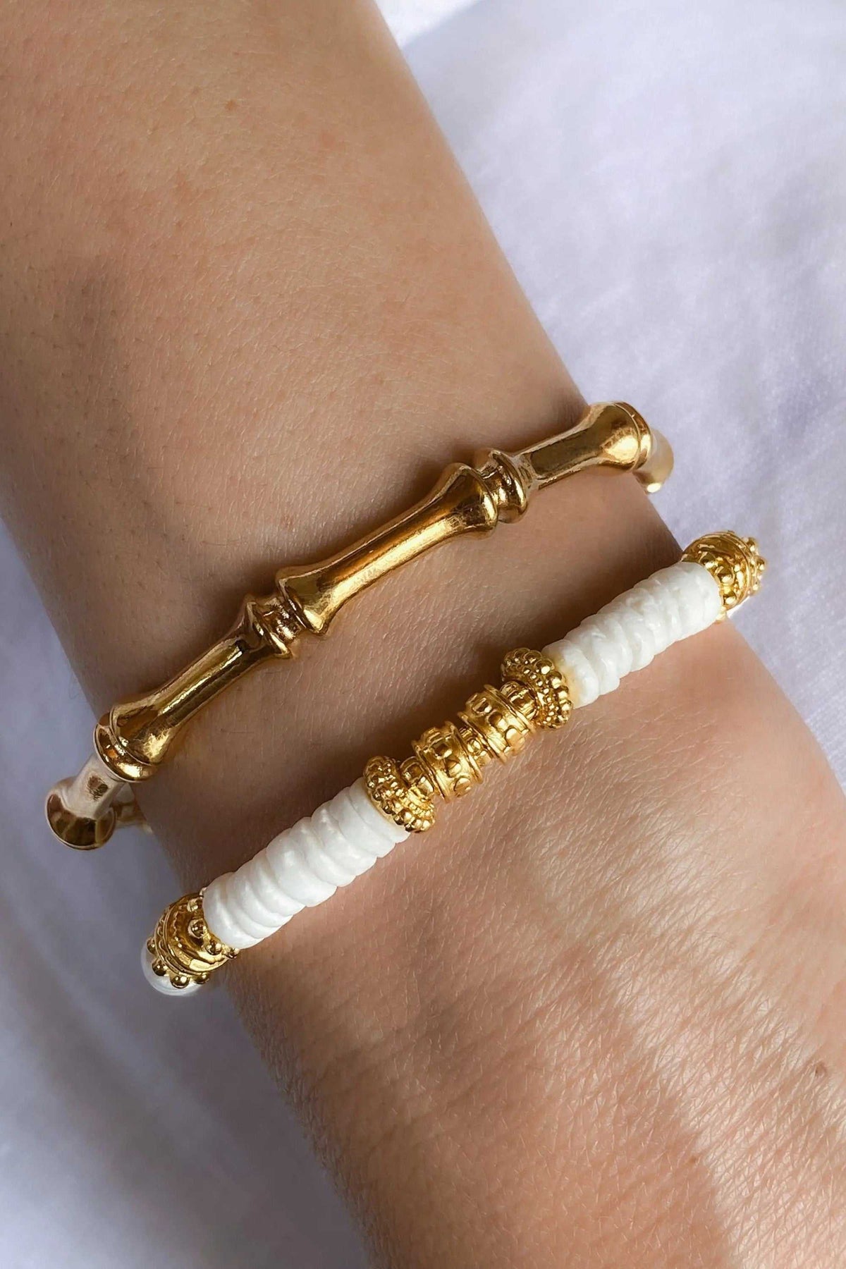 Bamboo pattern bracelet in shiny gold-tone metal, with a slim bamboo-inspired segmented design worn beside a white beaded bracelet