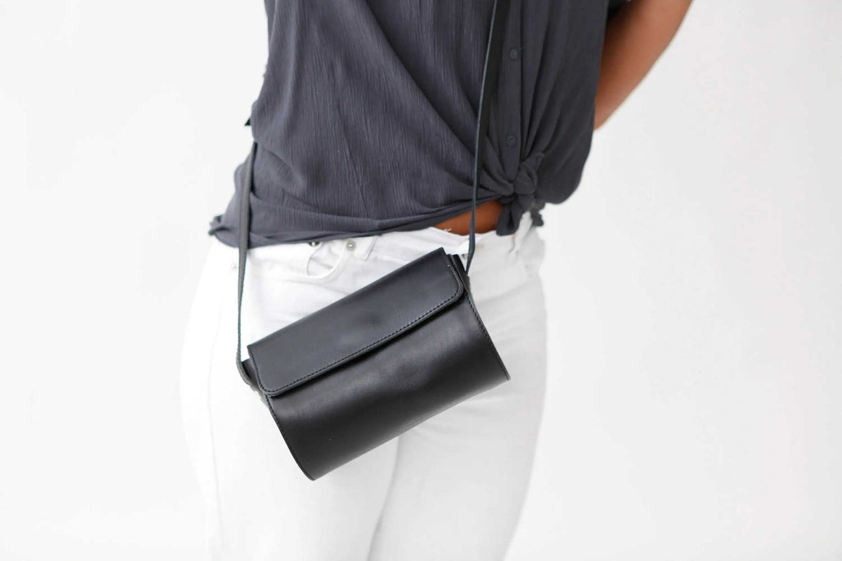Barrel Bag in black leather with a curved cylinder shape, slim shoulder strap and folded magnetic flap closure