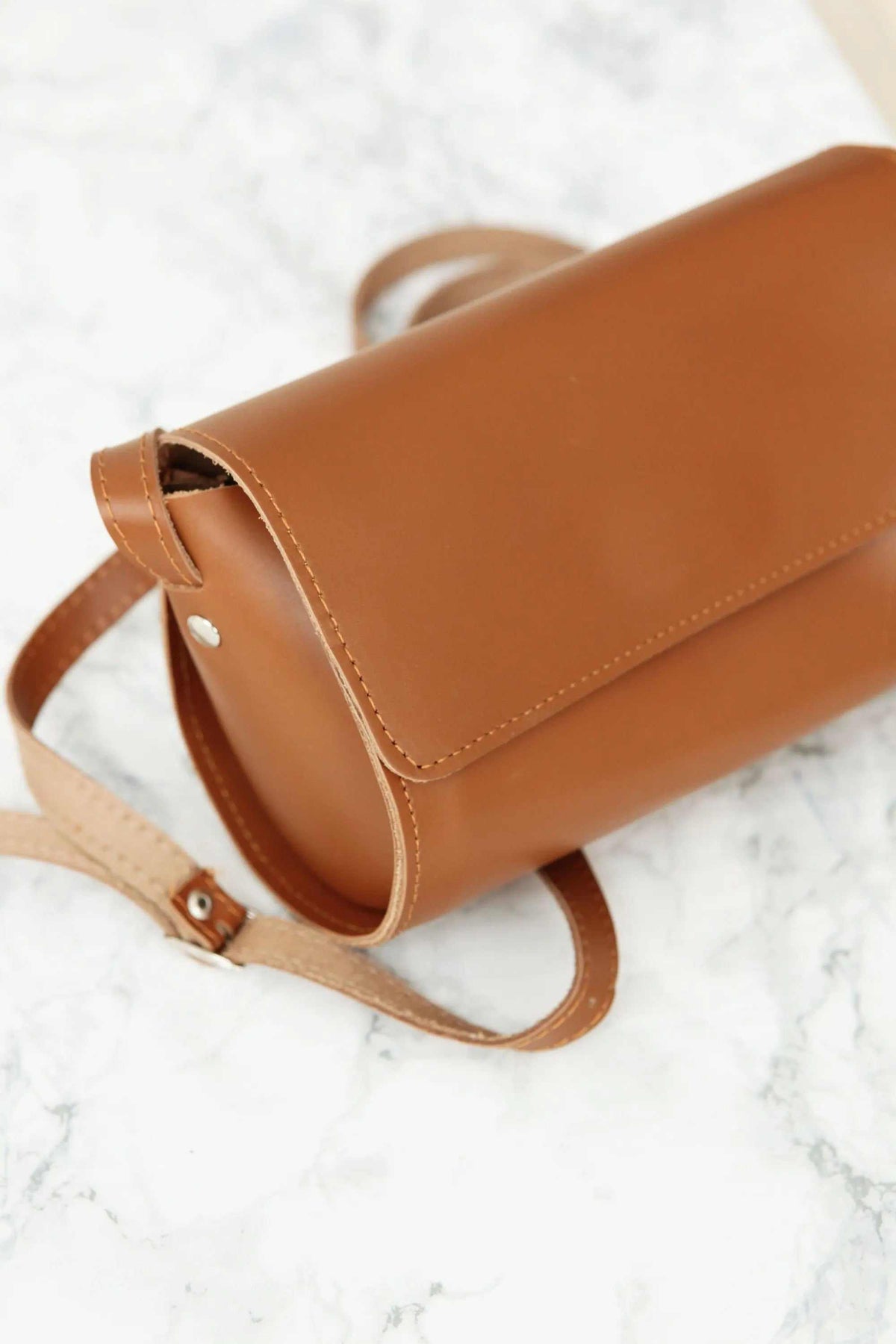 Barrel Bag in warm camel full-grain leather with a smooth finish, cylindrical shape, flap closure and adjustable strap