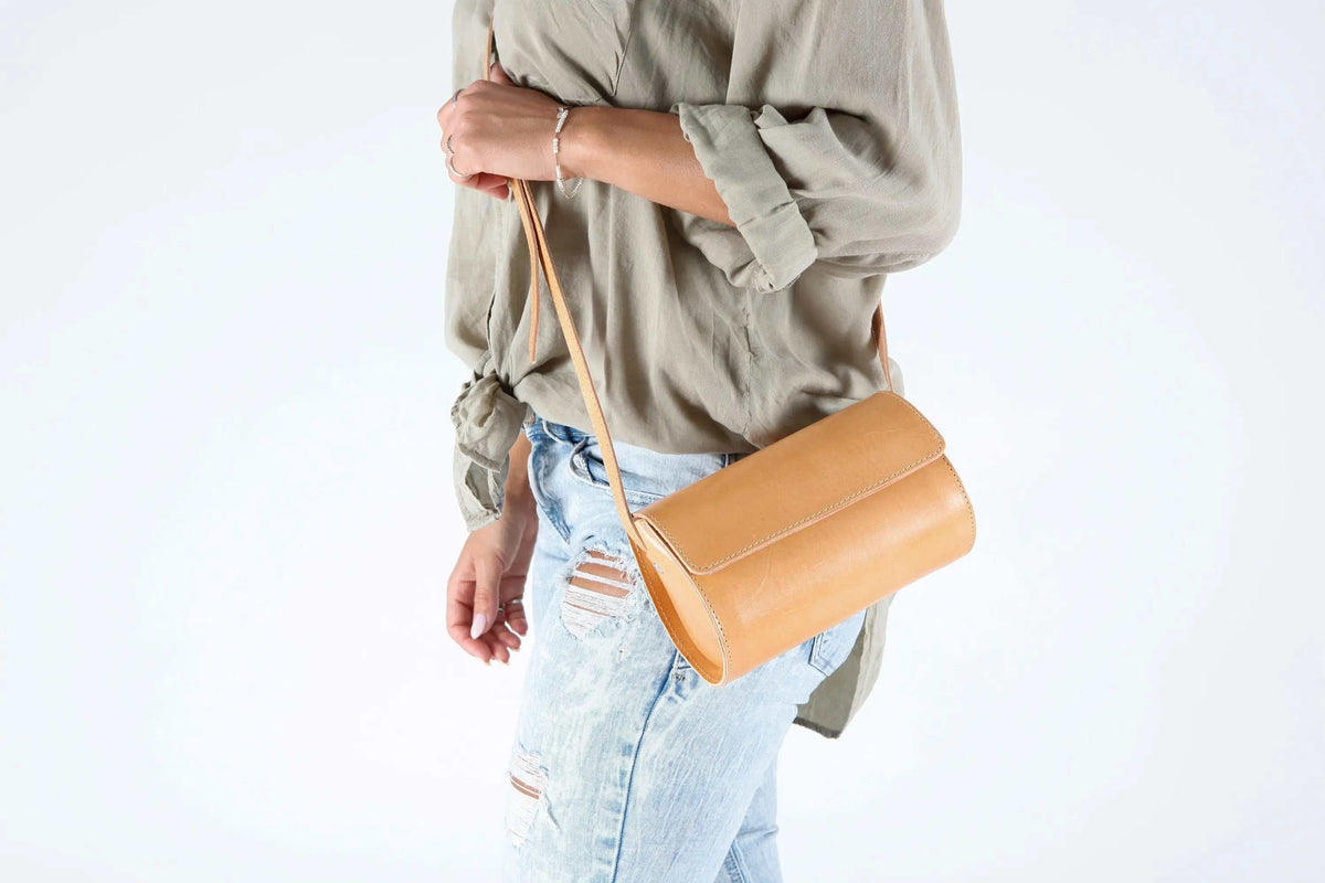 Barrel Bag in smooth camel leather with a compact cylinder shape, curved flap closure and slim adjustable strap