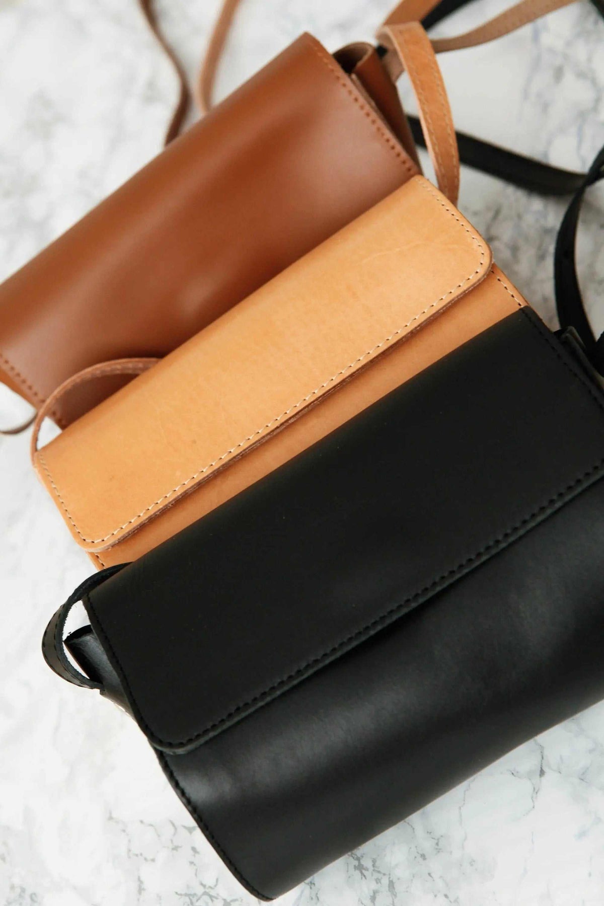 Barrel Bag in smooth brown, camel and black leather, shown as three flap-top shoulder bags with adjustable straps.