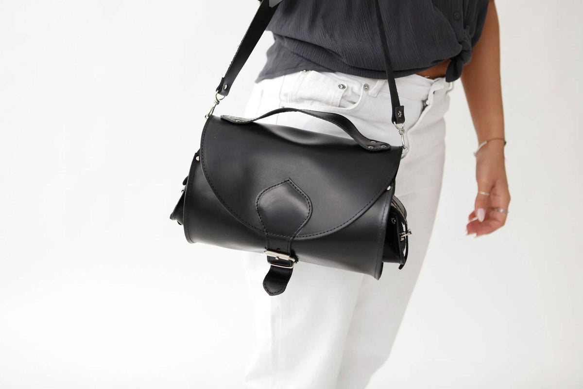 BARREL BAG with pockets in smooth black leather, with a curved flap, metal buckles and an adjustable shoulder strap