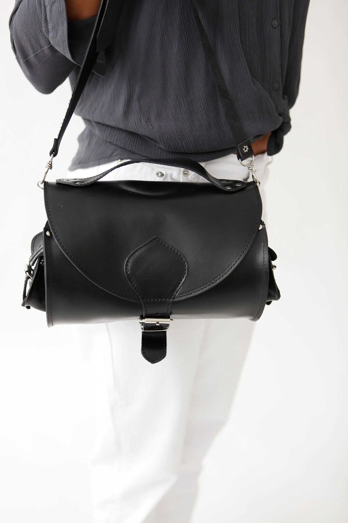 BARREL BAG with pockets in black leather, featuring a rounded cylinder shape, flap closure, metal buckle and side pockets