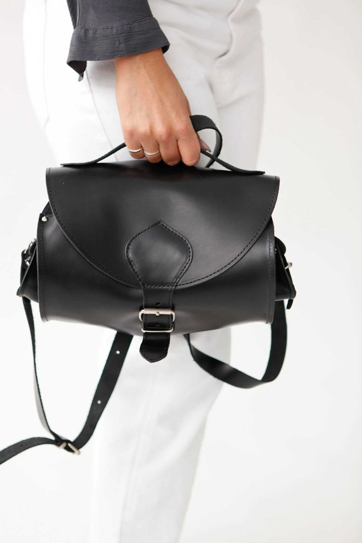 BARREL BAG with pockets in black full-grain leather, featuring flap closure, top handle, buckle, and shoulder strap