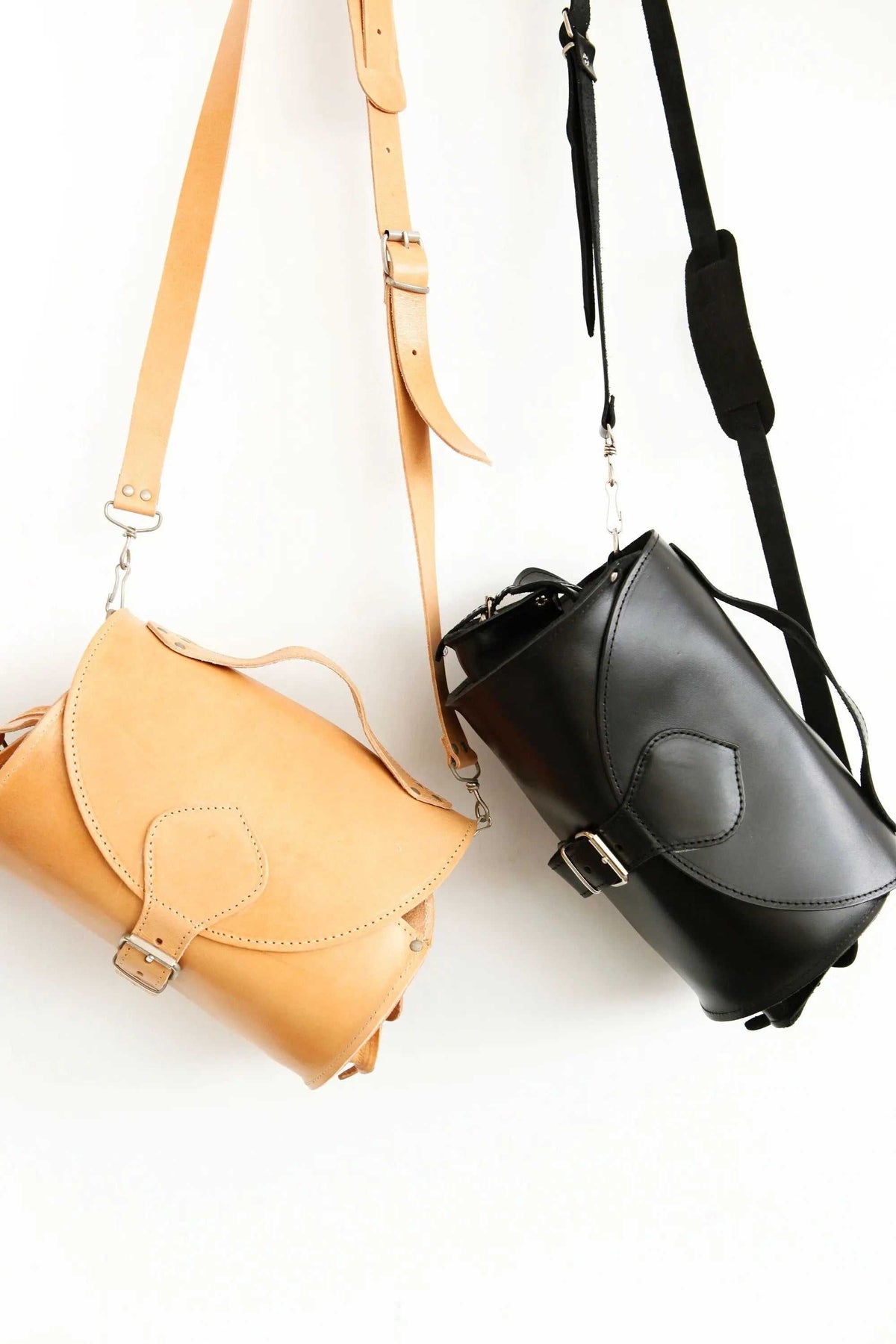 BARREL BAG with pockets in natural tan and black leather, featuring curved flap closures, buckles and long shoulder straps
