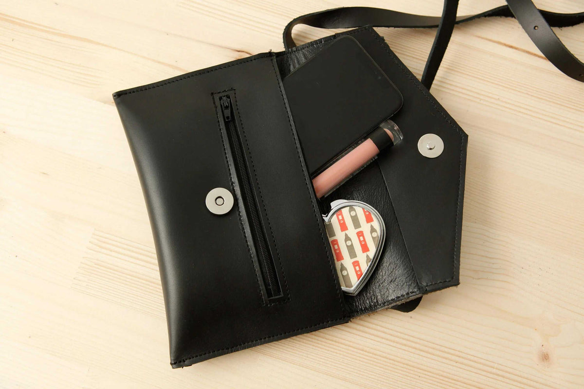 Belt bag in black leather, opened to show a zip pocket, snap closures and compact compartments for essentials.