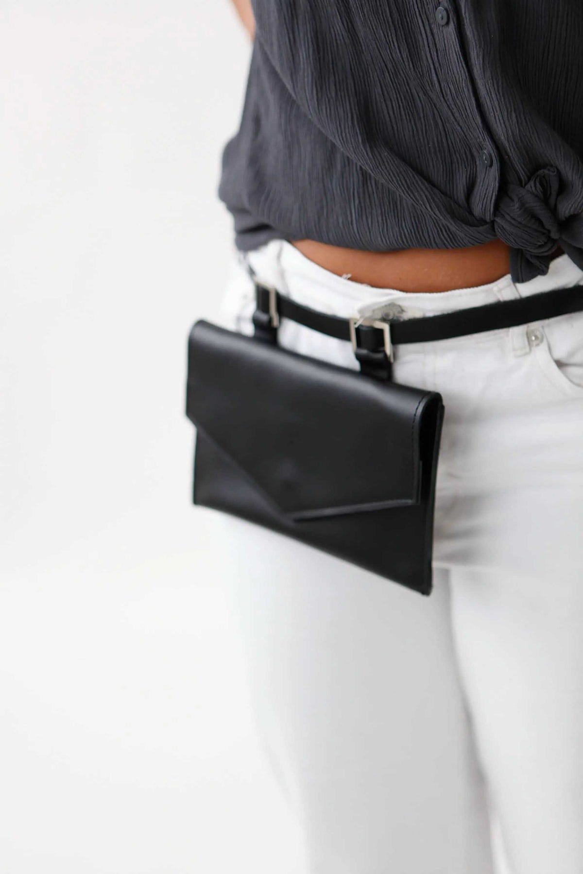 belt bag in black leather with a sleek rectangular envelope-style flap and slim belt attachment