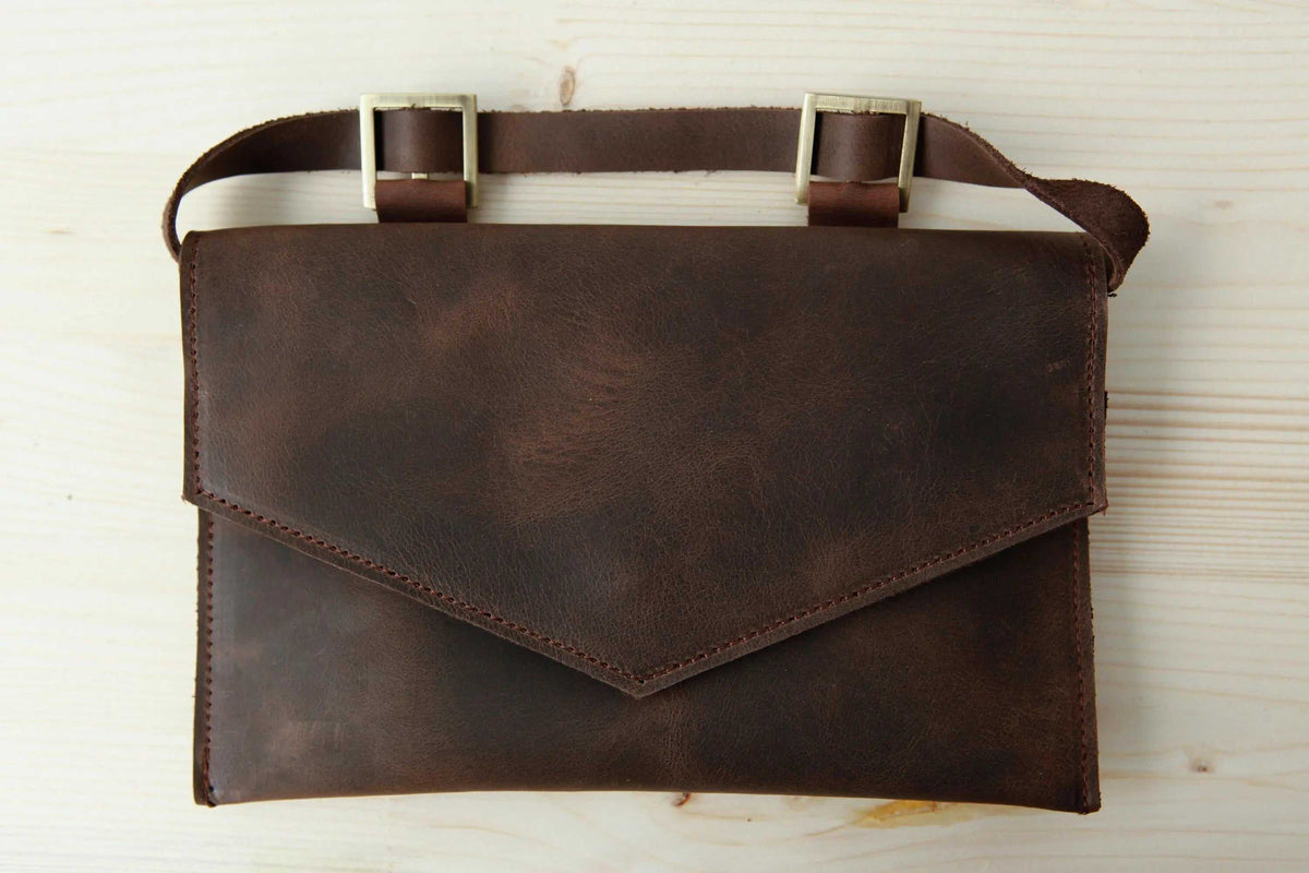 Belt bag in dark brown full-grain leather with a geometric flap, adjustable strap and metal buckles