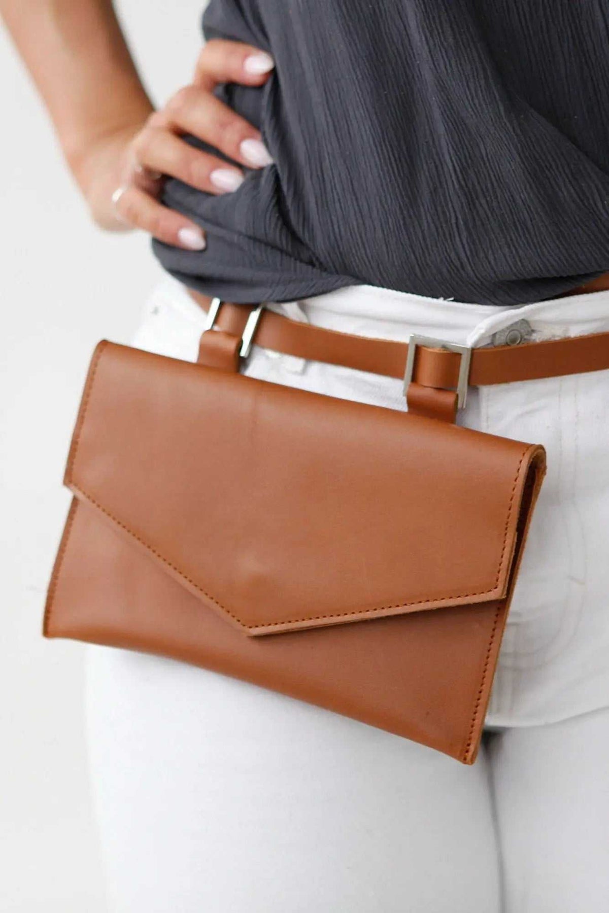belt bag in smooth tan leather with a wide envelope-style flap, worn on a brown waist strap with metal loops