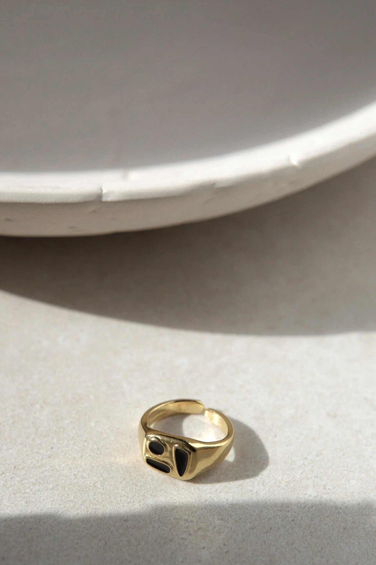 Black Forms Stamp RING, a gold-tone adjustable signet ring with two black oval stones set in a sculpted face