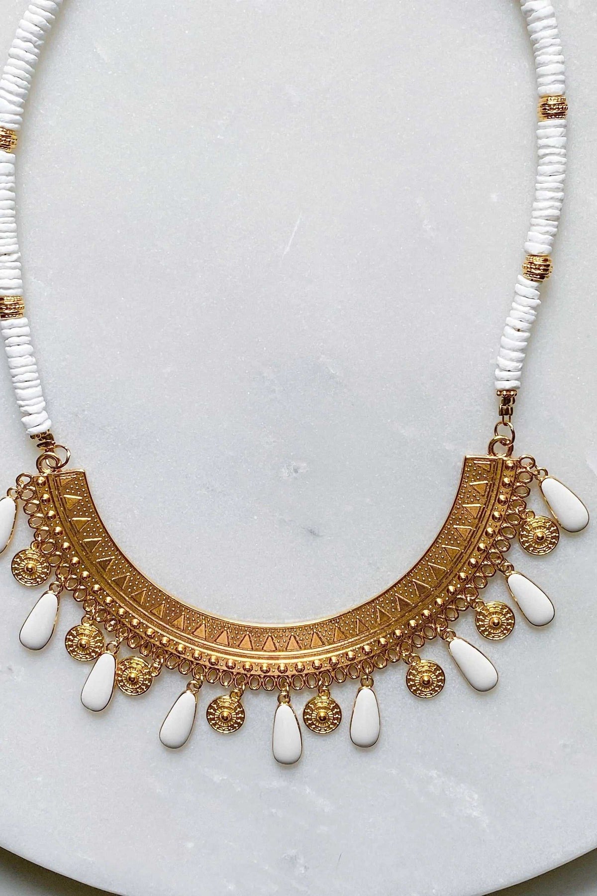 Boho chic necklace with white shell beads, gold-tone etched collar pendant, and dangling white enamel charms