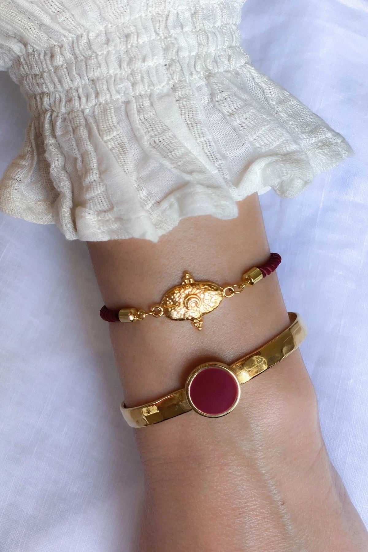 Bracelet femme or with a polished gold-tone band and round burgundy resin center, paired with a delicate charm bracelet