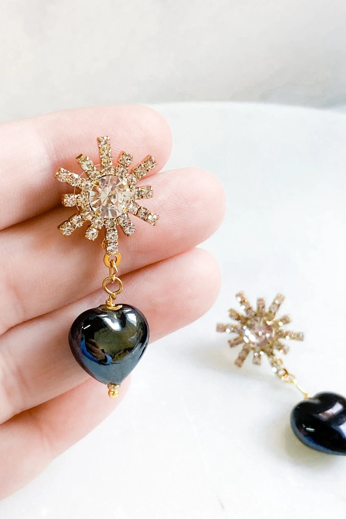 Crystal star earrings with gold-tone crystal sunburst studs and glossy black heart charms dangling below