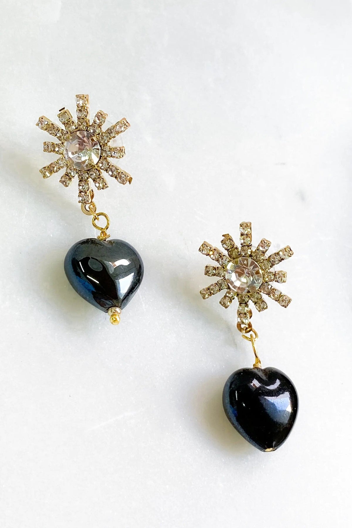 Crystal star earrings with gold-tone rhinestone starburst tops and dangling glossy black heart charms.