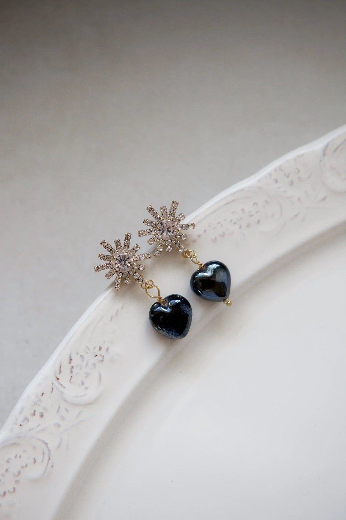 Crystal star earrings with gold-toned rhinestone starbursts and glossy black heart charms dangling below