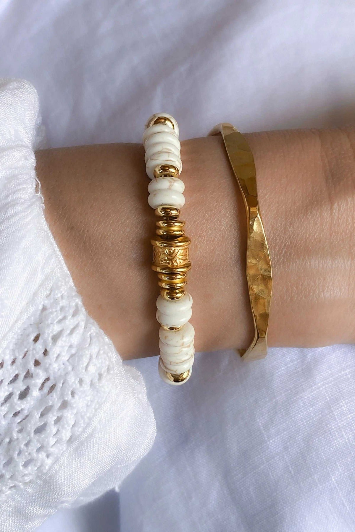 Delicate Hammered Bracelet in gold-tone metal with an uneven faceted surface, worn beside a white shell-bead bracelet