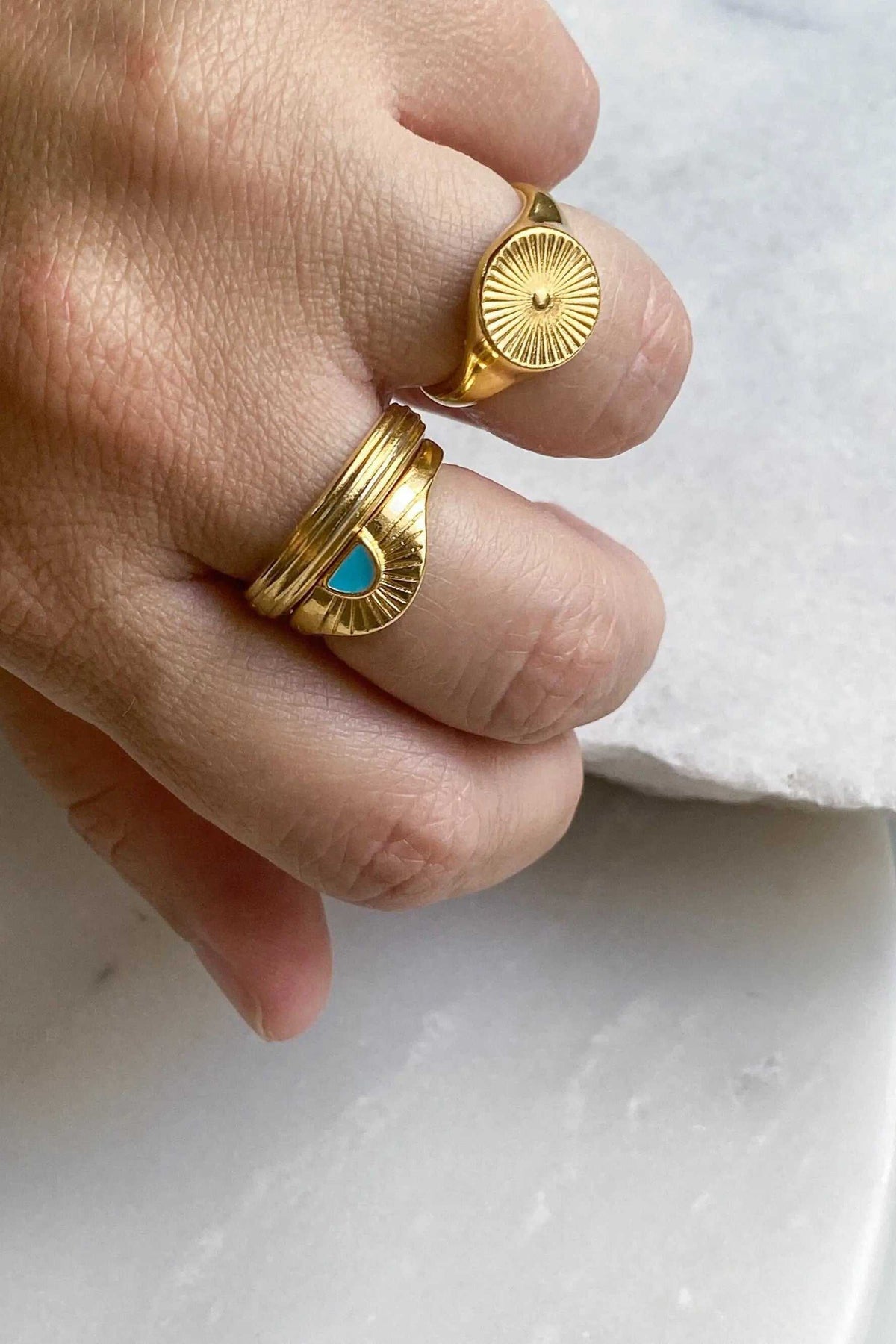 DELOS RING in gold-tone metal with a raised sunburst medallion and ridged rays, worn on a finger