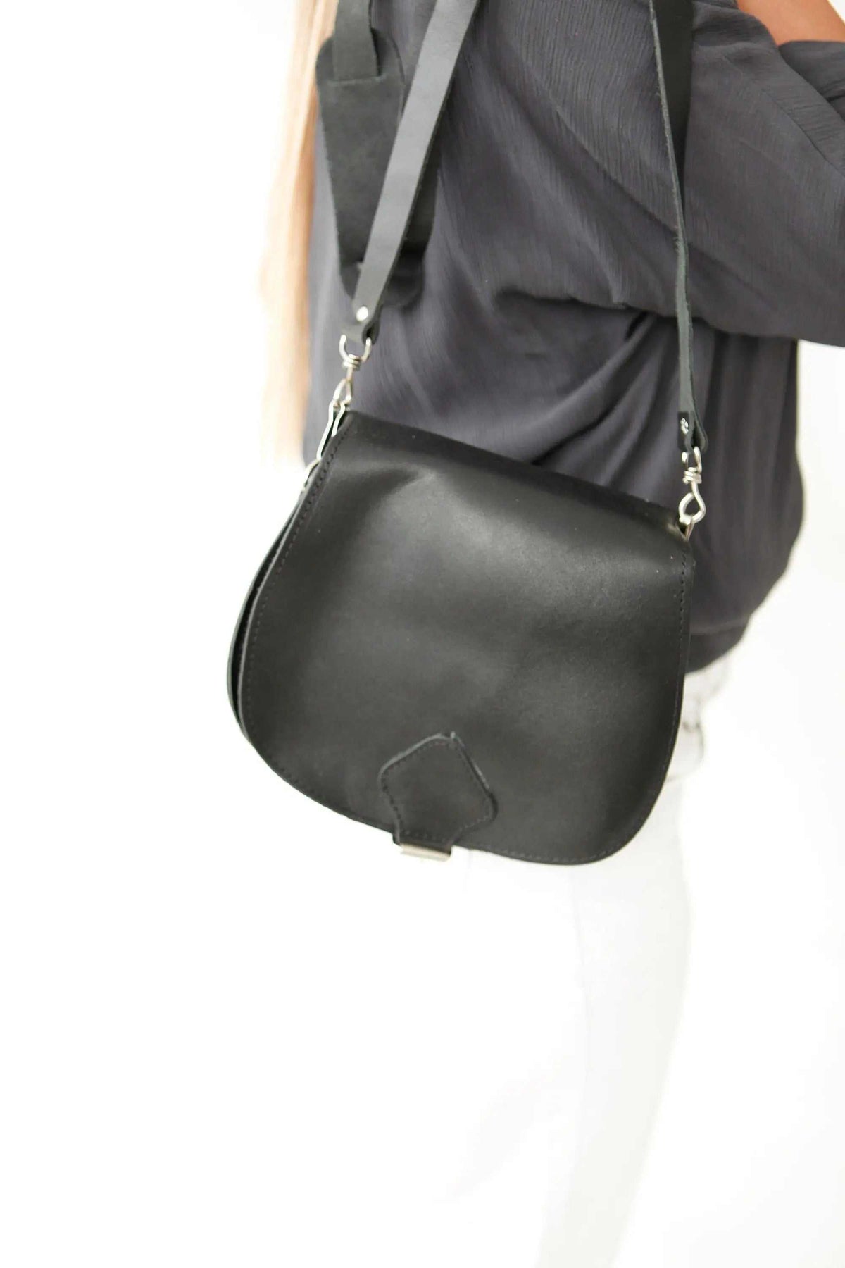 DIONE saddle shoulder bag in black leather, with a smooth curved flap, adjustable strap and metal clasps