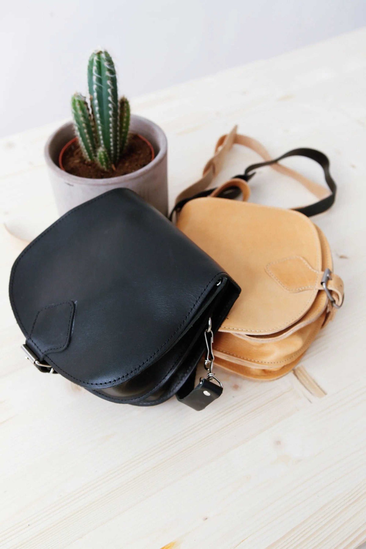 DIONE saddle shoulder bag in black and natural leather with rounded shape, adjustable strap and buckle details