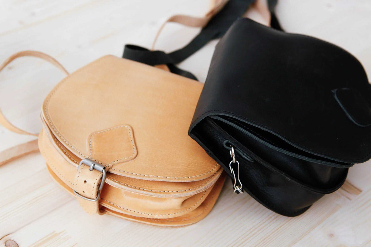 DIONE saddle shoulder bag in natural tan and black leather, with rounded flaps, stitched edges and buckle closures